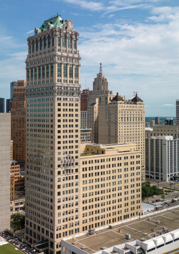Hoher historischer Bürohochhaus mit grünem Dach in Innenstadt, umgeben von weiteren Gebäuden und blauem Himmel.